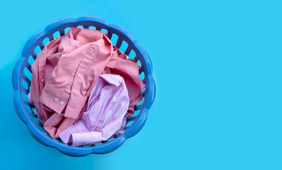 Clothes in a laundry basket on blue background. Copy space