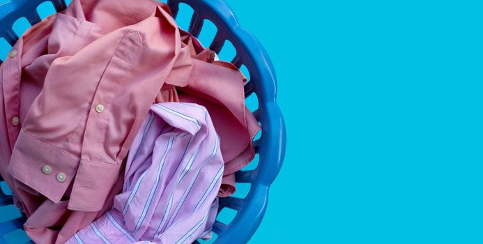 Clothes in a laundry basket on blue background. Copy space