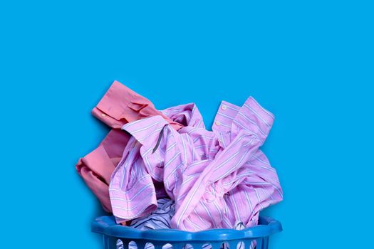 Clothes with a laundry basket on blue background. Copy space