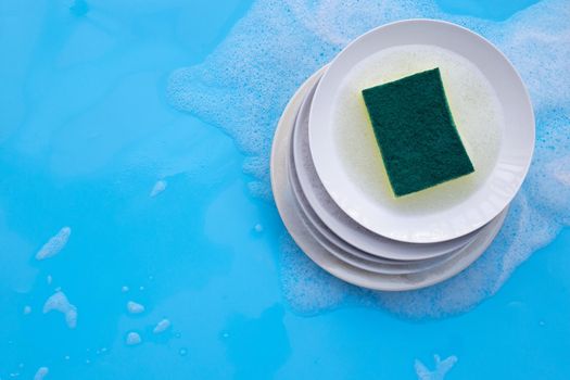 Washing dishes concept. wet blue with soapy foam background.