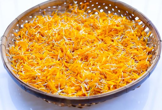 Marigold flower petals in wooden bamboo threshing basket on white background. 