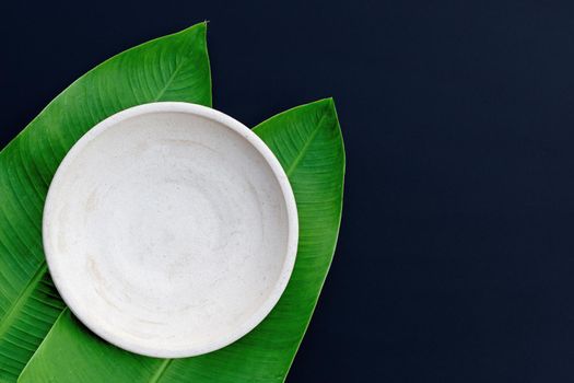 Empty white plate on tropical banana leaves on dark background. Top view