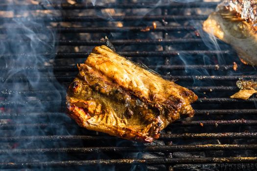 Grilled mackerel fish with smoke on a charcoal barbecue grill.