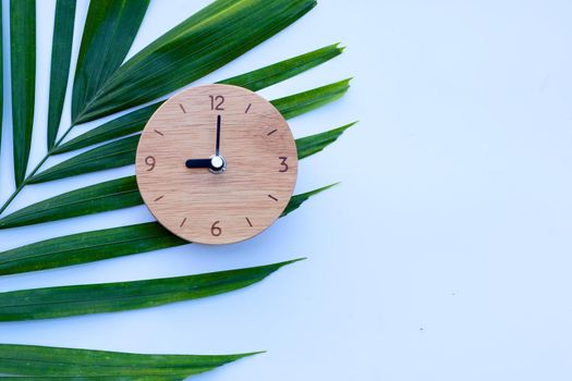 Wooden clock on green leaves on white background. Copy space