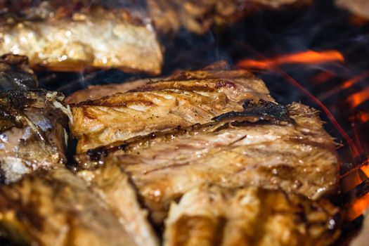 Grilled mackerel fish with smoke on a charcoal barbecue grill.