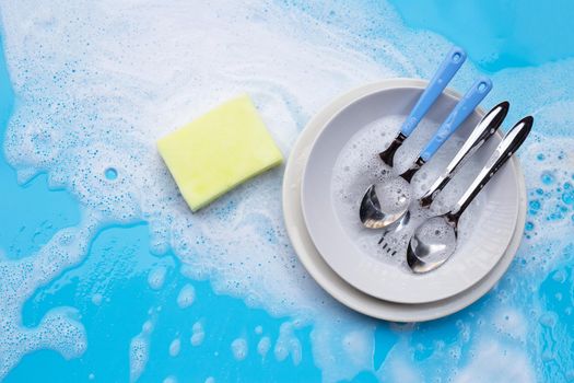 Washing dishes concept. wet blue with soapy foam background.
