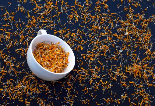 White cup with dry marigold flower petals on dark background. Herbal tea concept.