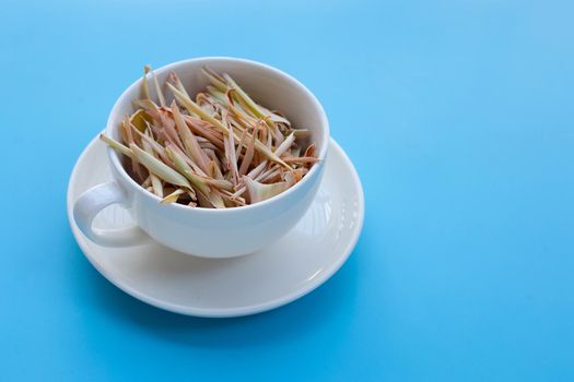 Organic dried lemongrass in white cup on blue background. Herbal tea concept
