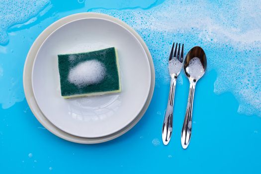 Washing dishes on wet blue background with soapy foam.