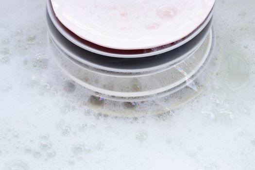 Washing dishes on wet background with soapy foam.