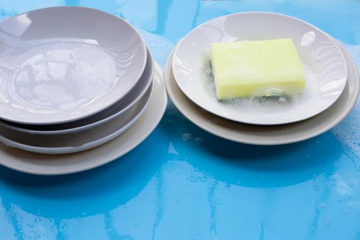 Washing dishes on wet blue background with soapy foam.