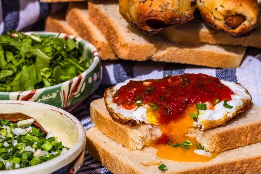 Rustic composition with sausages rolls, fried egg on toast bread, different bowls with sauce and chopped vegetables.