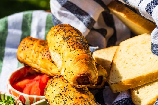 Sausages baked in dough sprinkled with salt and poppy seeds in a rustic composition. Sausages rolls, delicious homemade pastries.