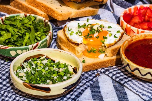 Rustic composition with sausages rolls, fried egg on toast bread, different bowls with sauce and chopped vegetables.