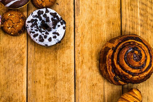 Colorful donuts on wooden table. Sweet icing sugar food with glazed sprinkles, doughnut with chocolate frosting. Top view with copy space