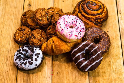 Colorful donuts on wooden table. Sweet icing sugar food with glazed sprinkles, doughnut with chocolate frosting. Top view with copy space