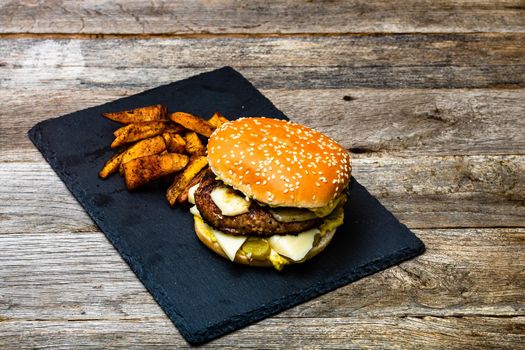 Homemade fresh tasty cheese burger and fried potatoes on a wooden table