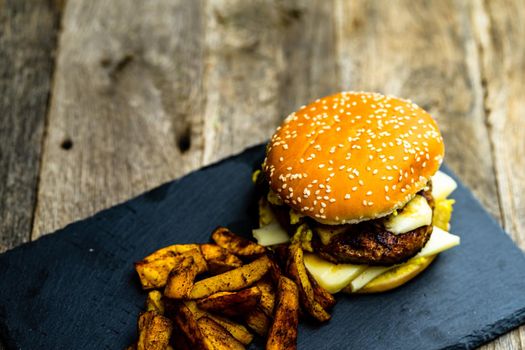 Homemade fresh tasty cheese burger and fried potatoes on a wooden table