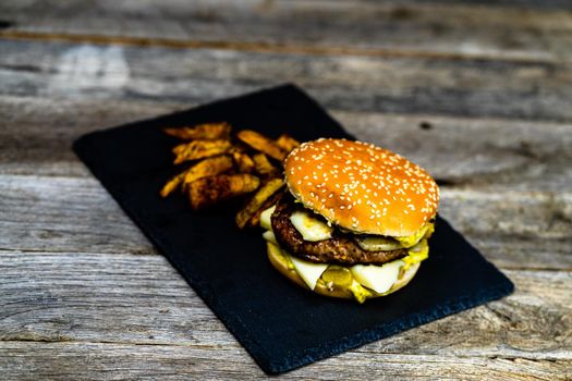 Homemade fresh tasty cheese burger and fried potatoes on a wooden table