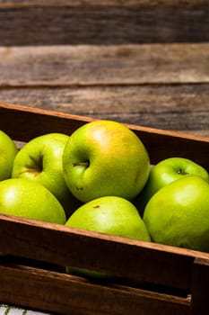 Wooden crate with ripe green apples on wooden table.