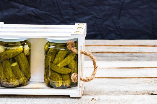 Wooden crate with glass jars with pickles isolated. Preserved food concept, canned vegetables isolated in a rustic composition.