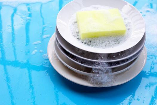 Washing dishes on wet blue background with soapy foam.