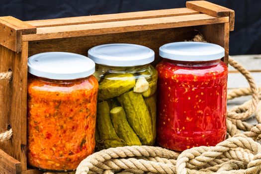 Wooden crate with glass jars with variety of canned vegetables isolated.