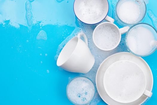 Washing used drinking glasses and cups on wet blue background with soapy foam