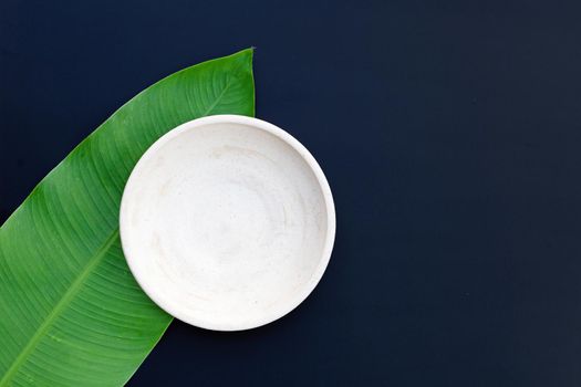 Empty white plate on tropical banana leaves on dark background. Top view