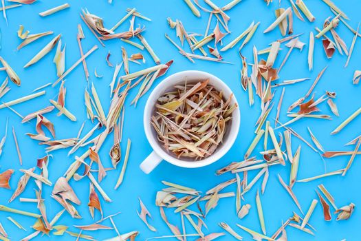 Organic dried lemongrass in white cup on blue background. Herbal tea concept