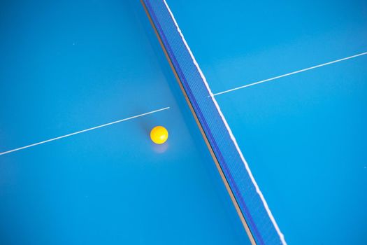 Net of table tennis ping pong with yellow ball on blue background.