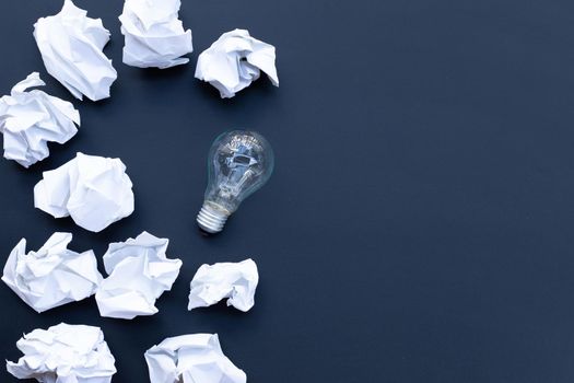 Light bulb with white crumpled paper balls on dark background. Ideas and creative thinking concept. Top view