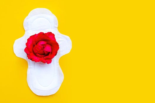 White sanitary napkin with red rose on yellow background. 