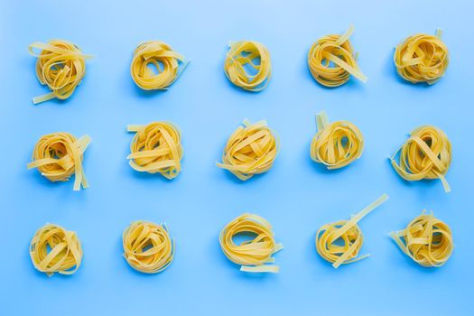 Uncooked Italian pasta tagliatelle nest on blue background. Copy space