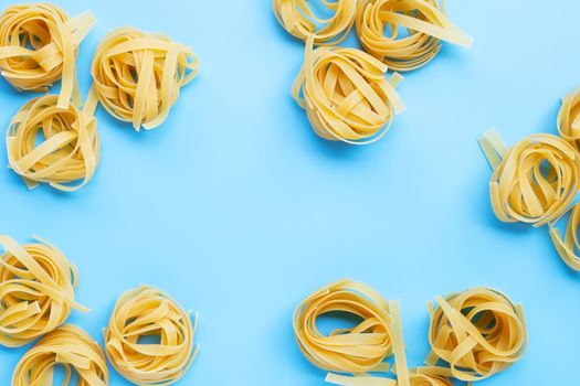 Uncooked Italian pasta tagliatelle nest on blue background. Copy space