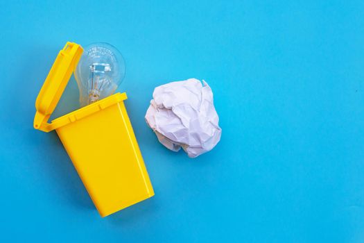 Yellow bin with light bulb and white crumpled paper on blue background. Ideas and creative thinking concept. Top view