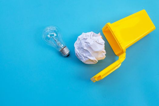Yellow bin with light bulb and white crumpled paper on blue background. Ideas and creative thinking concept. Top view