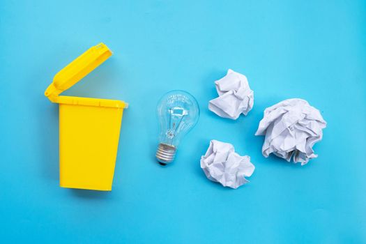 Yellow bin with light bulb and white crumpled paper on blue background. Ideas and creative thinking concept. Top view