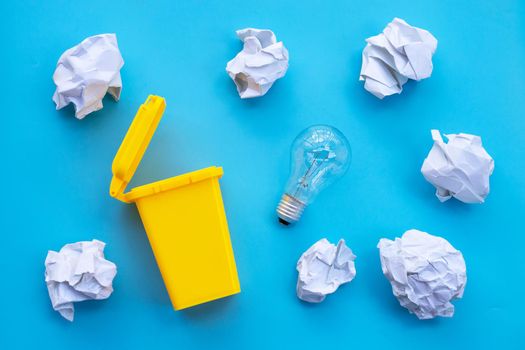 Yellow bin with light bulb and white crumpled paper on blue background. Ideas and creative thinking concept. Top view