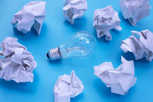 Light bulb with white crumpled paper on blue background. Ideas and creative thinking concept. Top view