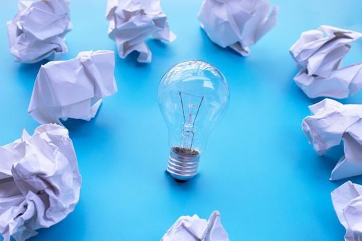 Light bulb with white crumpled paper on blue background. Ideas and creative thinking concept. Top view