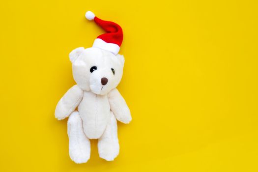 Toy bear wearing a santa hat on yellow background. Christmas holidays concept