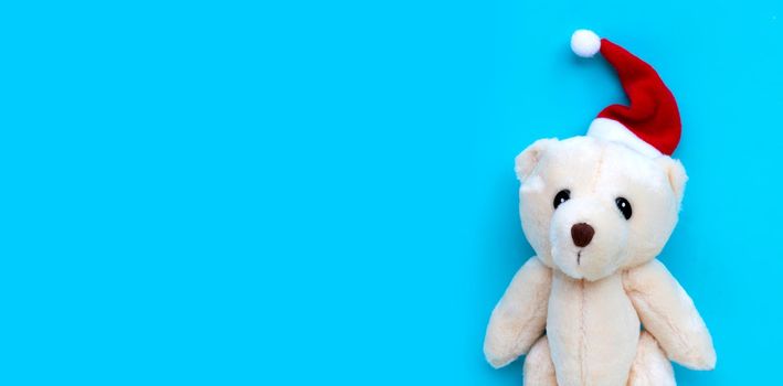 Toy bear wearing a santa hat on blue background. Christmas holidays concept