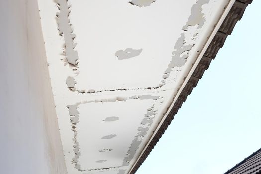 White color paint peeling off on ceiling house. Under the roof