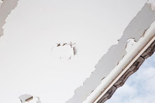 White color paint peeling off on ceiling house. Under the roof