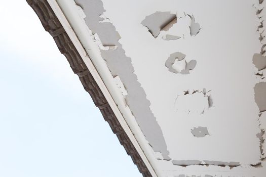 White color paint peeling off on ceiling house. Under the roof