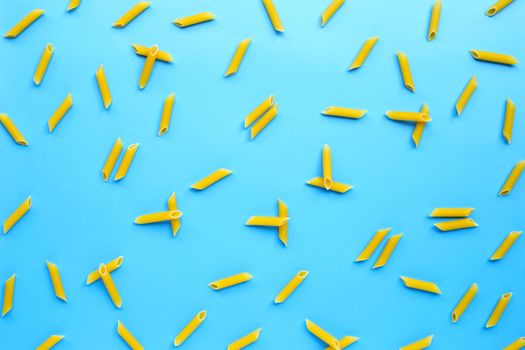 Uncooked penne pasta on blue background. Copy space