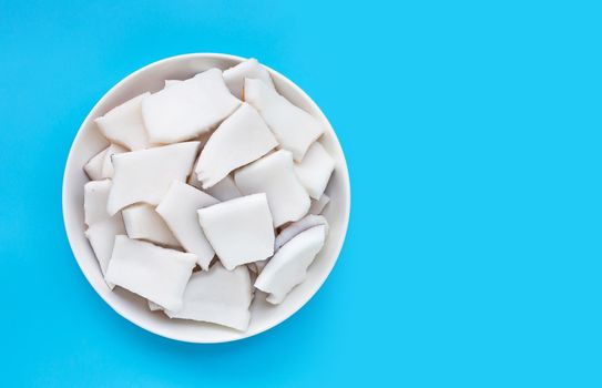 Coconut cut pieces in bowl on blue background. Copy space