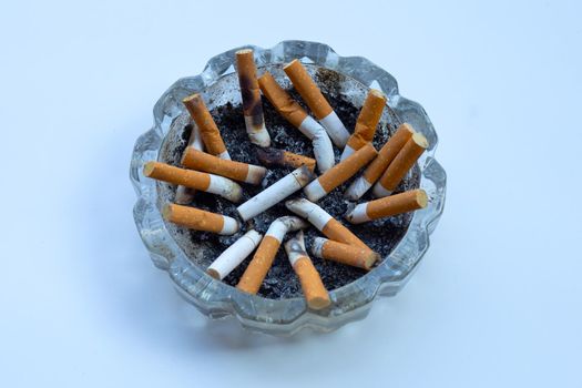 Cigarette butts in glass ashtray on white background.