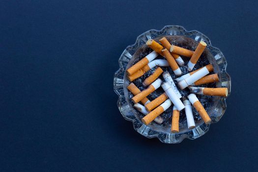 Cigarette butts in glass ashtray on dark background.